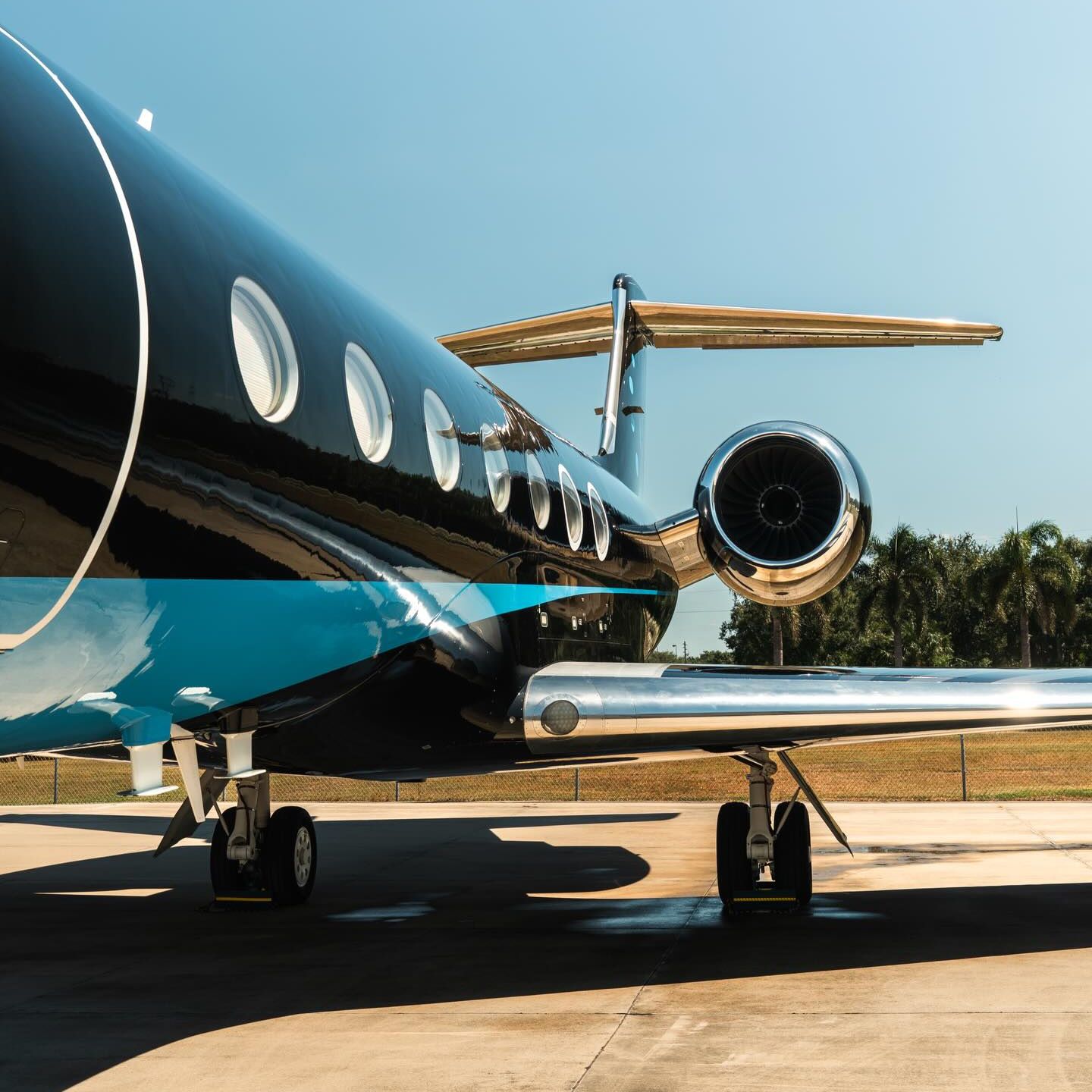 Black and blue private jet parked on tarmac on a sunny day.