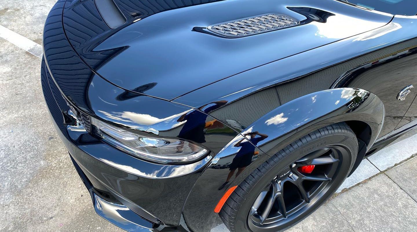 Black Dodge Challenger Hellcat, shiny exterior, red brake calipers, black wheels.