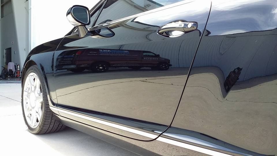 Black car with shiny finish reflecting a building and a vehicle; chrome trim.