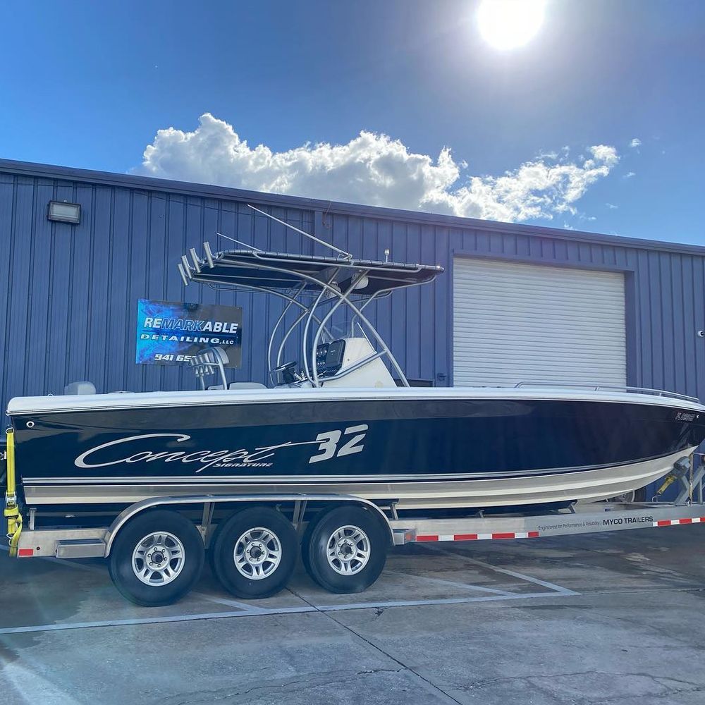 Black and white boat on trailer, blue building background, sunny sky. Boat is labeled 