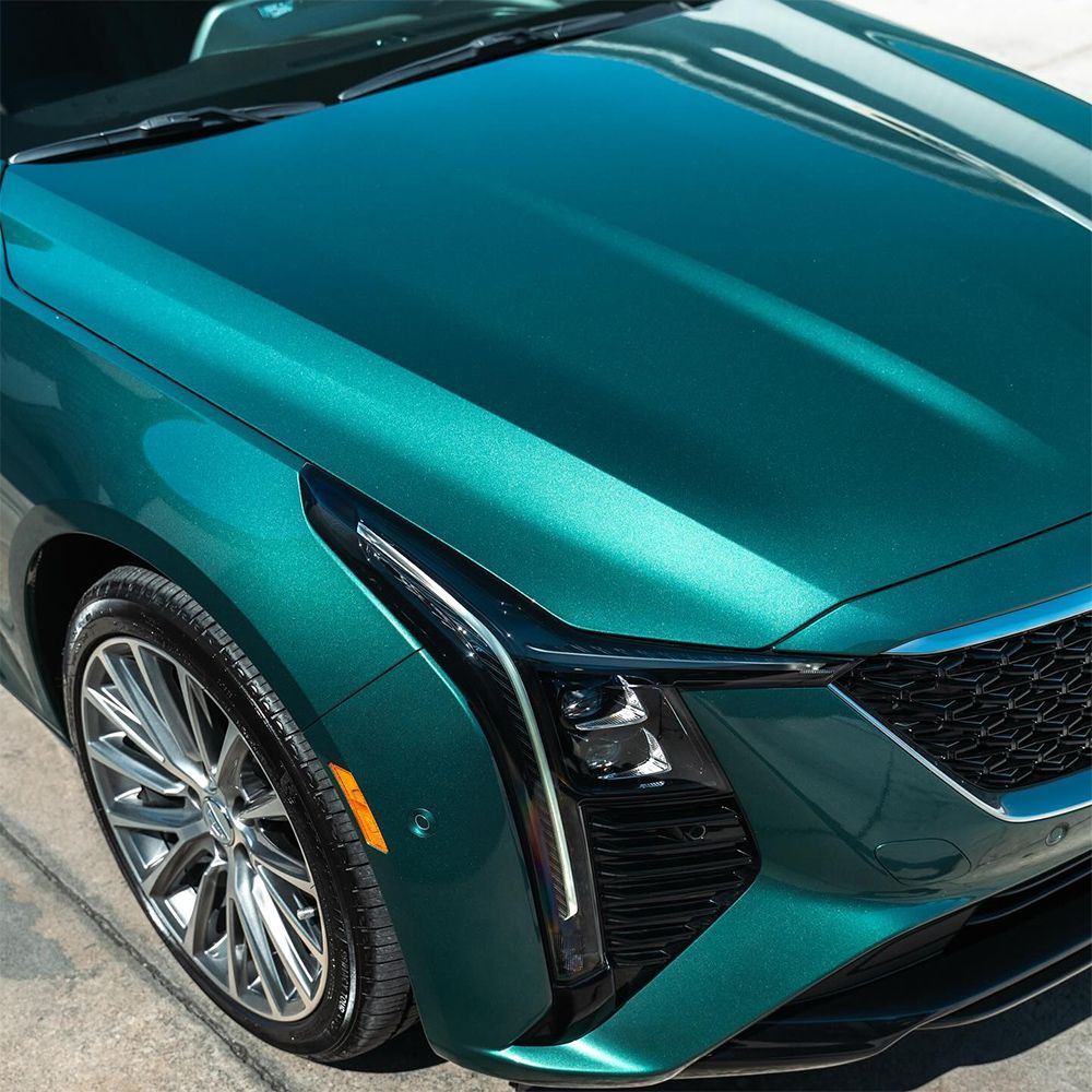 Green Cadillac car, close-up of front. Shiny paint, silver grill, and chrome wheels.