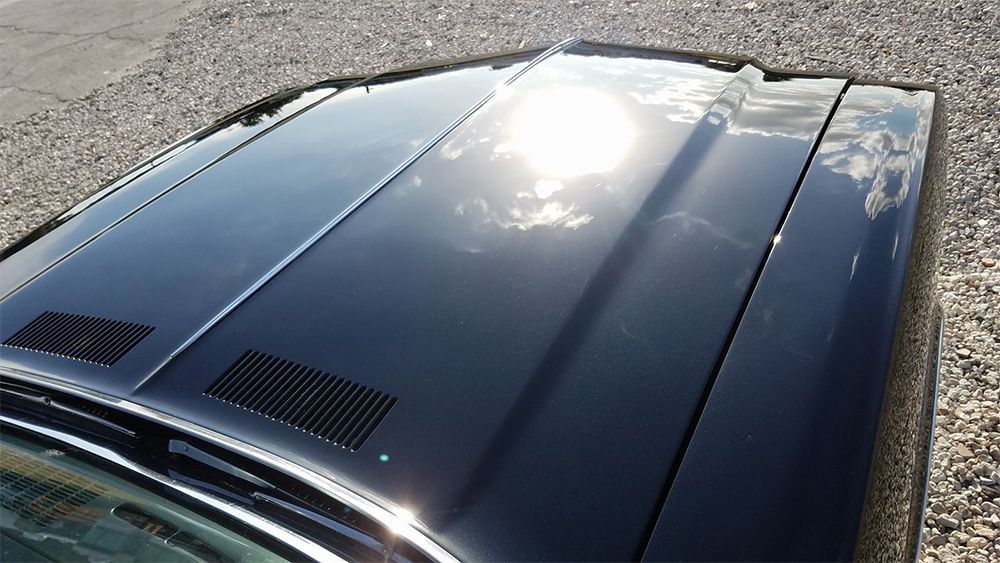 Black car hood with air vents reflecting sunlight.