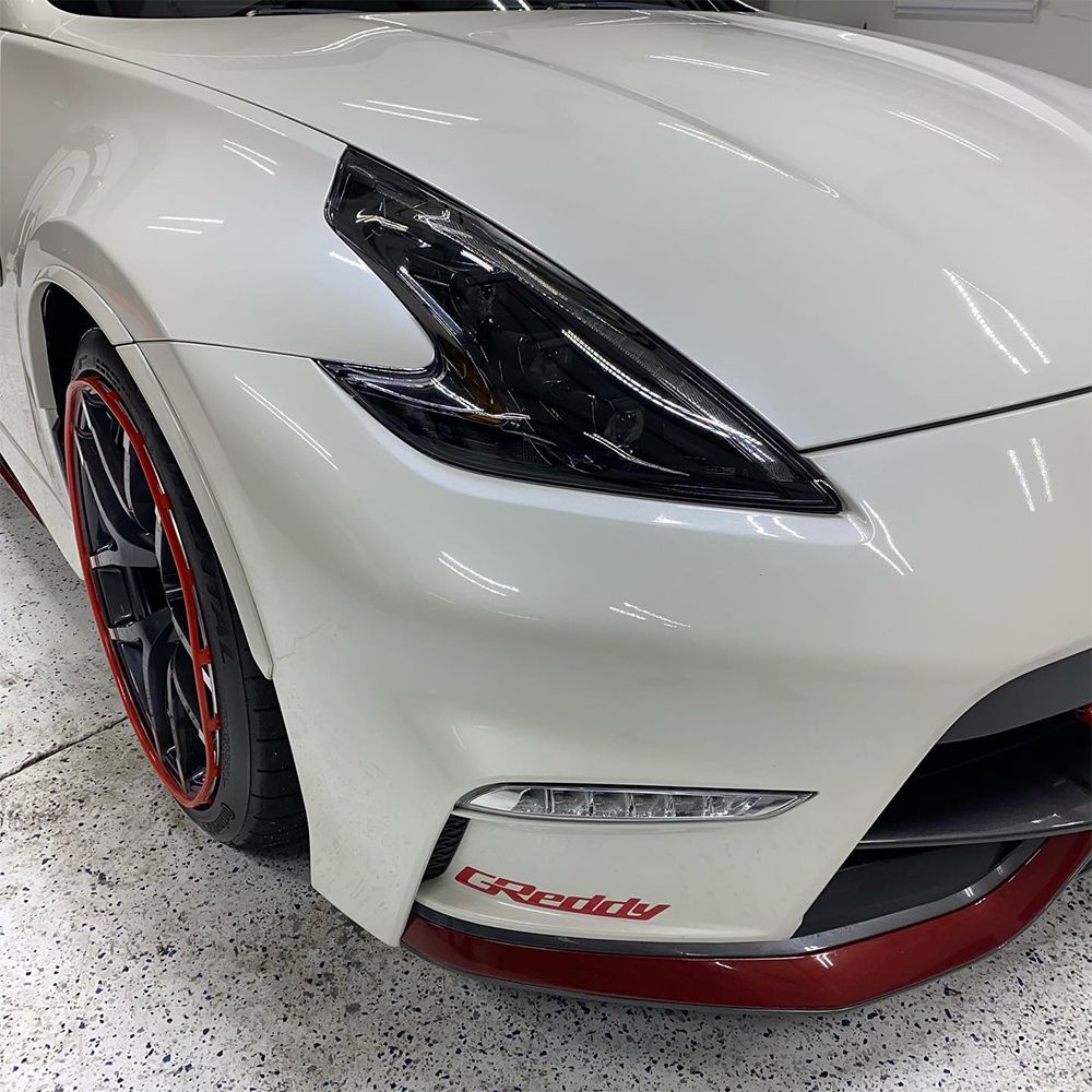 White Nissan 370Z sports car with black headlights, red accents on wheels and spoiler.