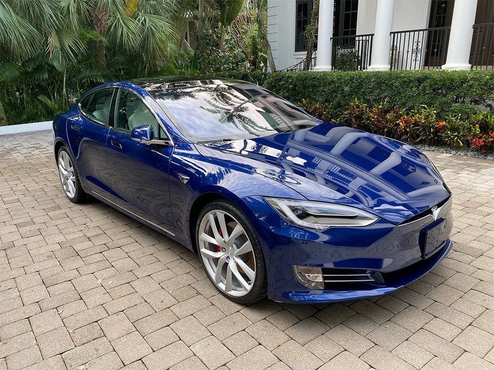 Blue Tesla Model S sedan parked on brick pavers in front of a house.
