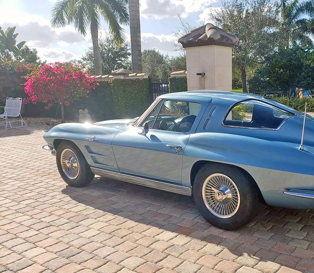 Blue classic Corvette parked on a brick driveway, sunny day.