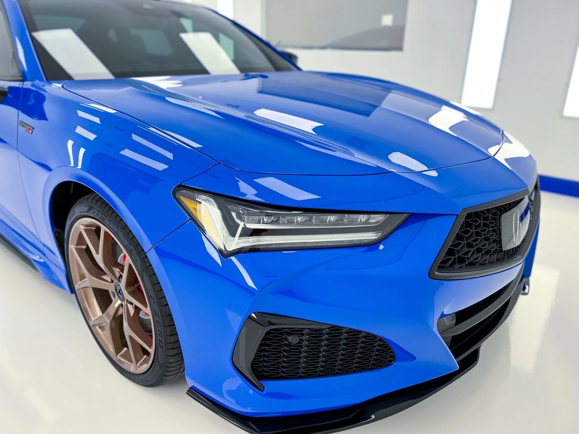Blue Acura TLX, front view, bronze wheels, black accents, indoors.