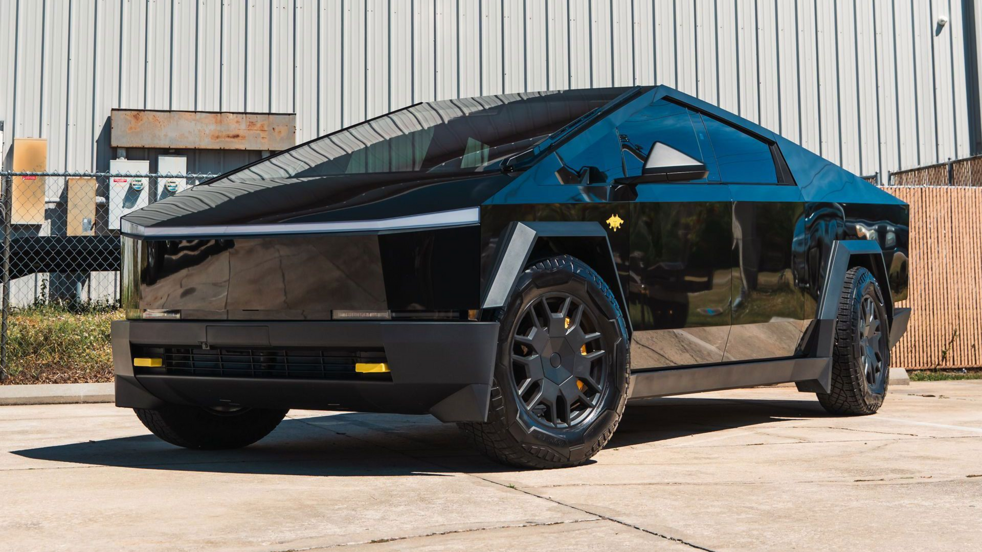 Tesla Cybertruck, black, parked on pavement, angled view, industrial background.