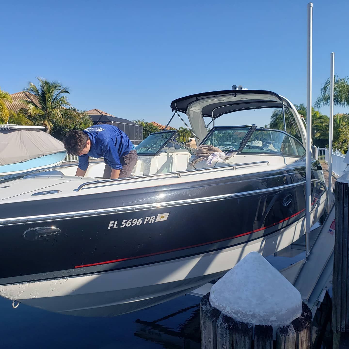 Man on a docked boat, cleaning the deck under a sunny sky.