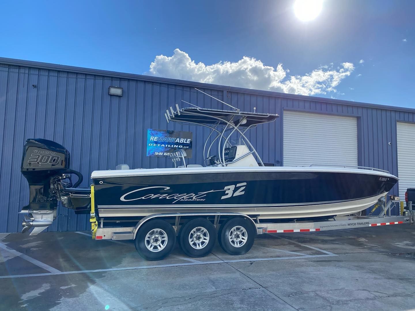 Black and white powerboat on a trailer in front of a blue building with white garage doors, sunny day.