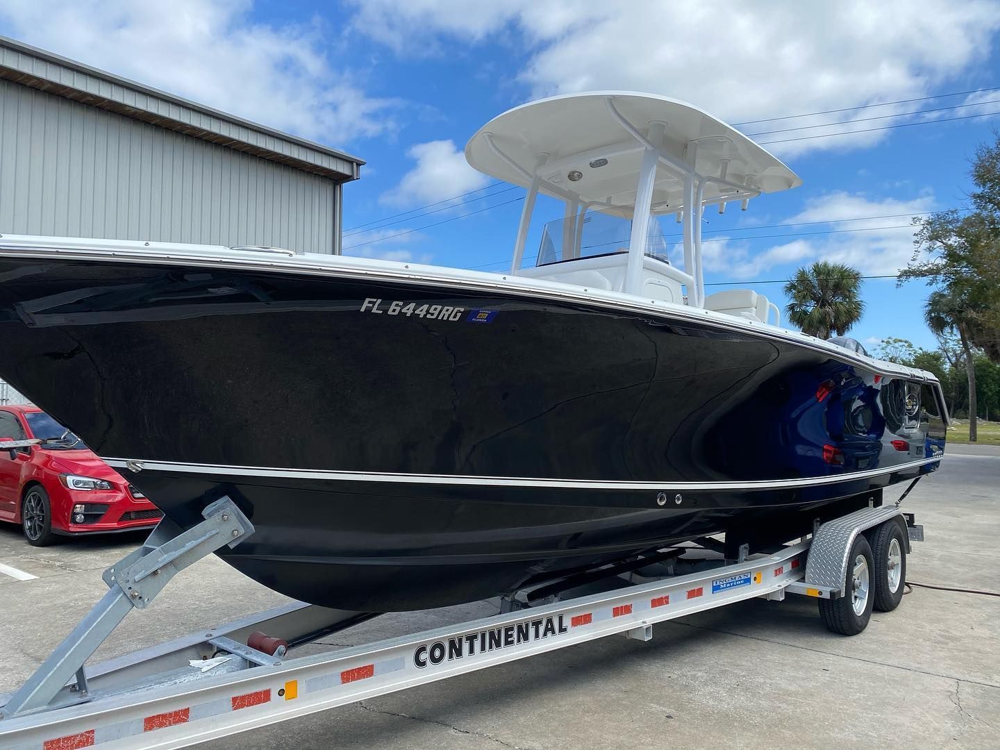 Dark blue boat on a trailer, parked outside a building, with white top.