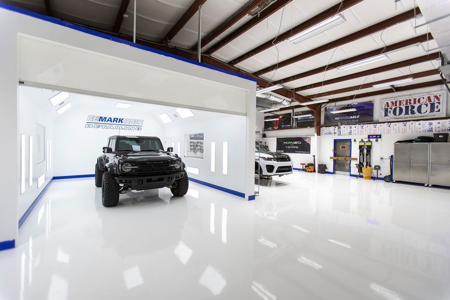 Black Jeep inside a bright white auto shop bay. Other vehicles and equipment are visible in the shop.