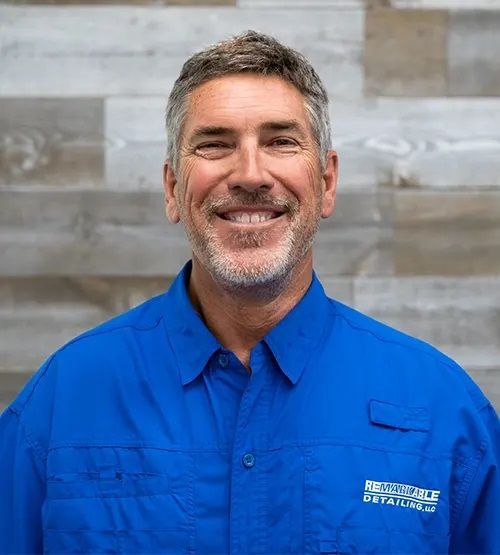Man smiling, wearing a blue shirt, in front of a wood-paneled wall.