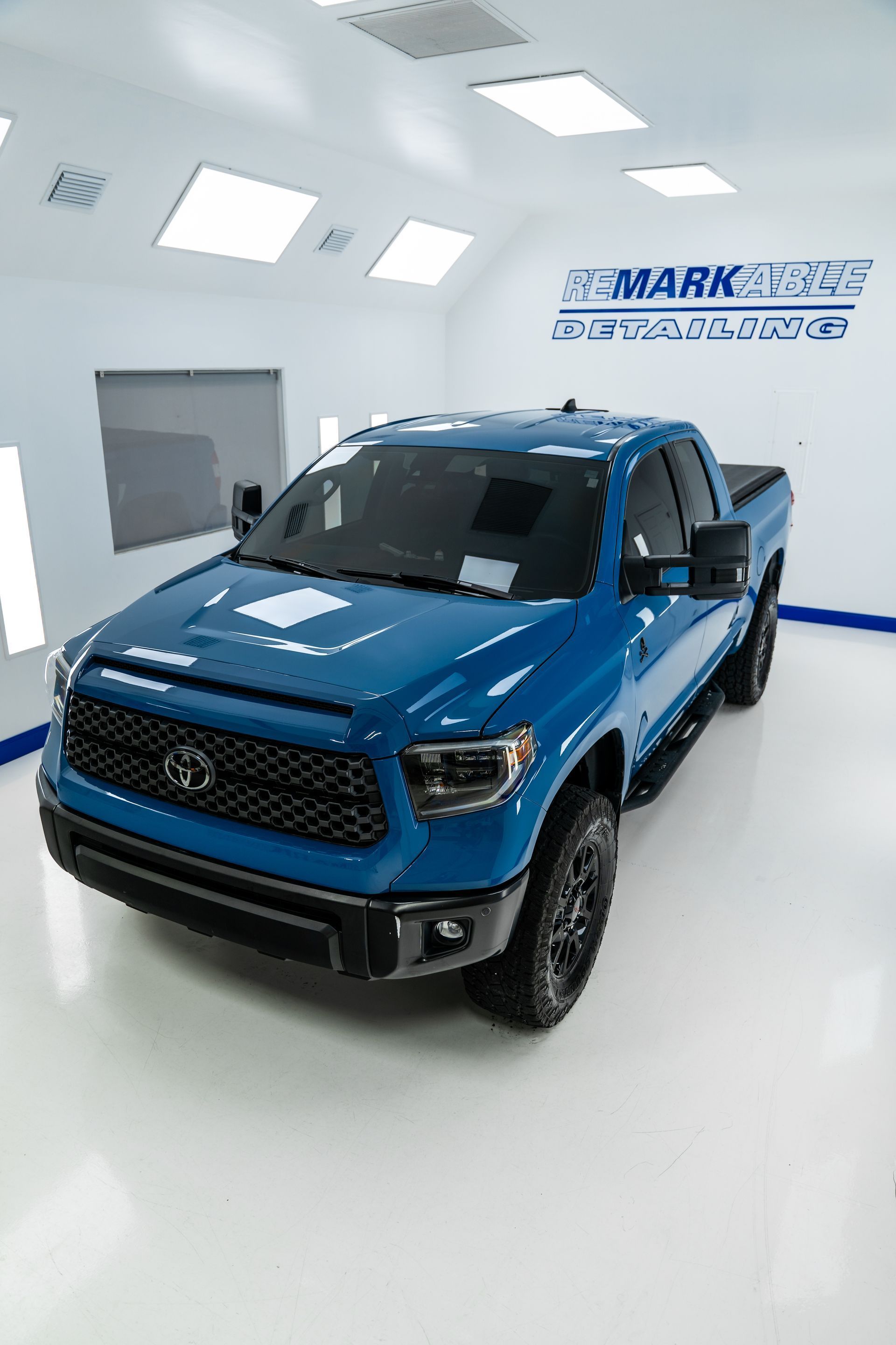 Blue Toyota Tundra pickup truck in a brightly lit showroom. Black grill and wheels.