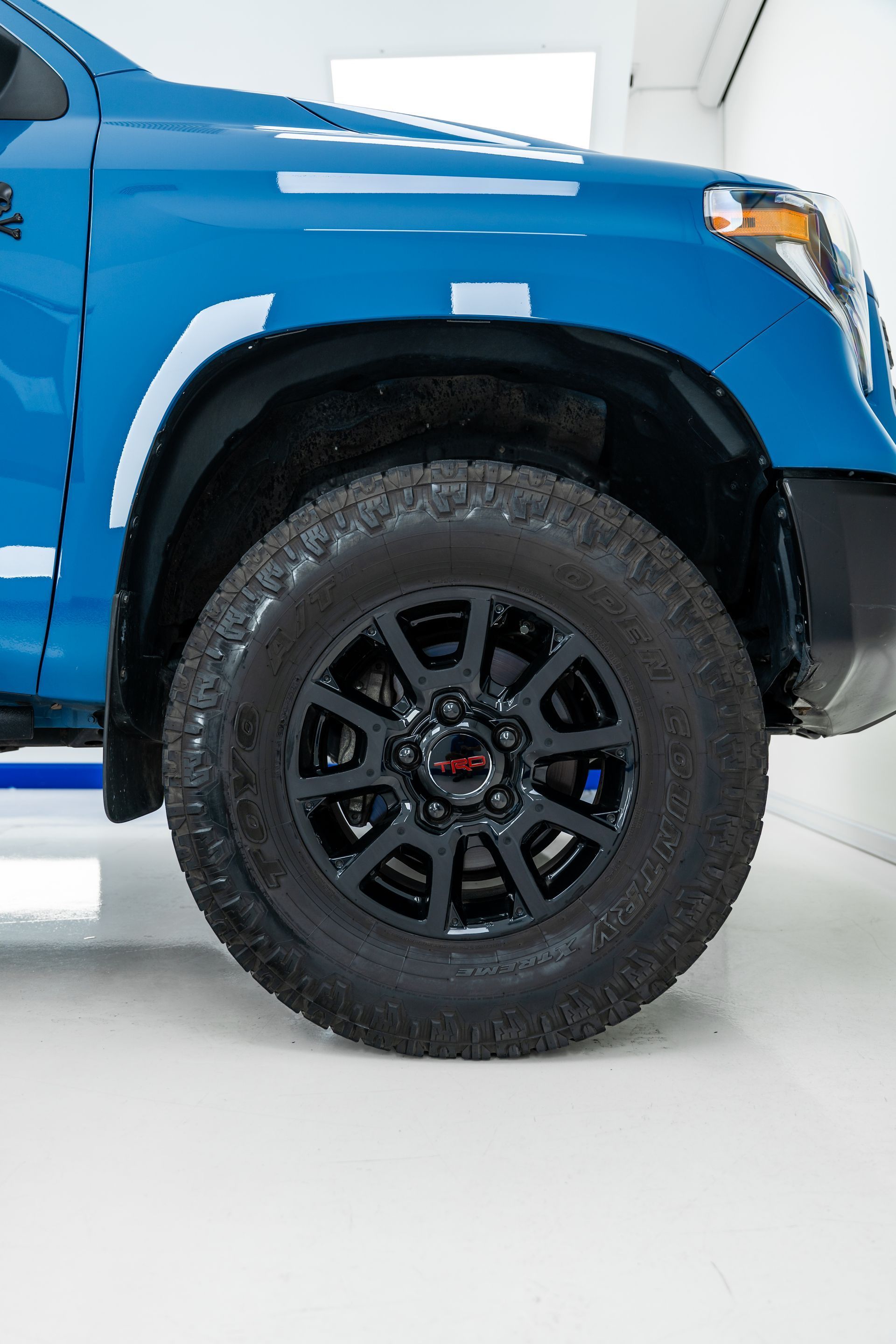 Blue Toyota truck front wheel with black rim and off-road tire.