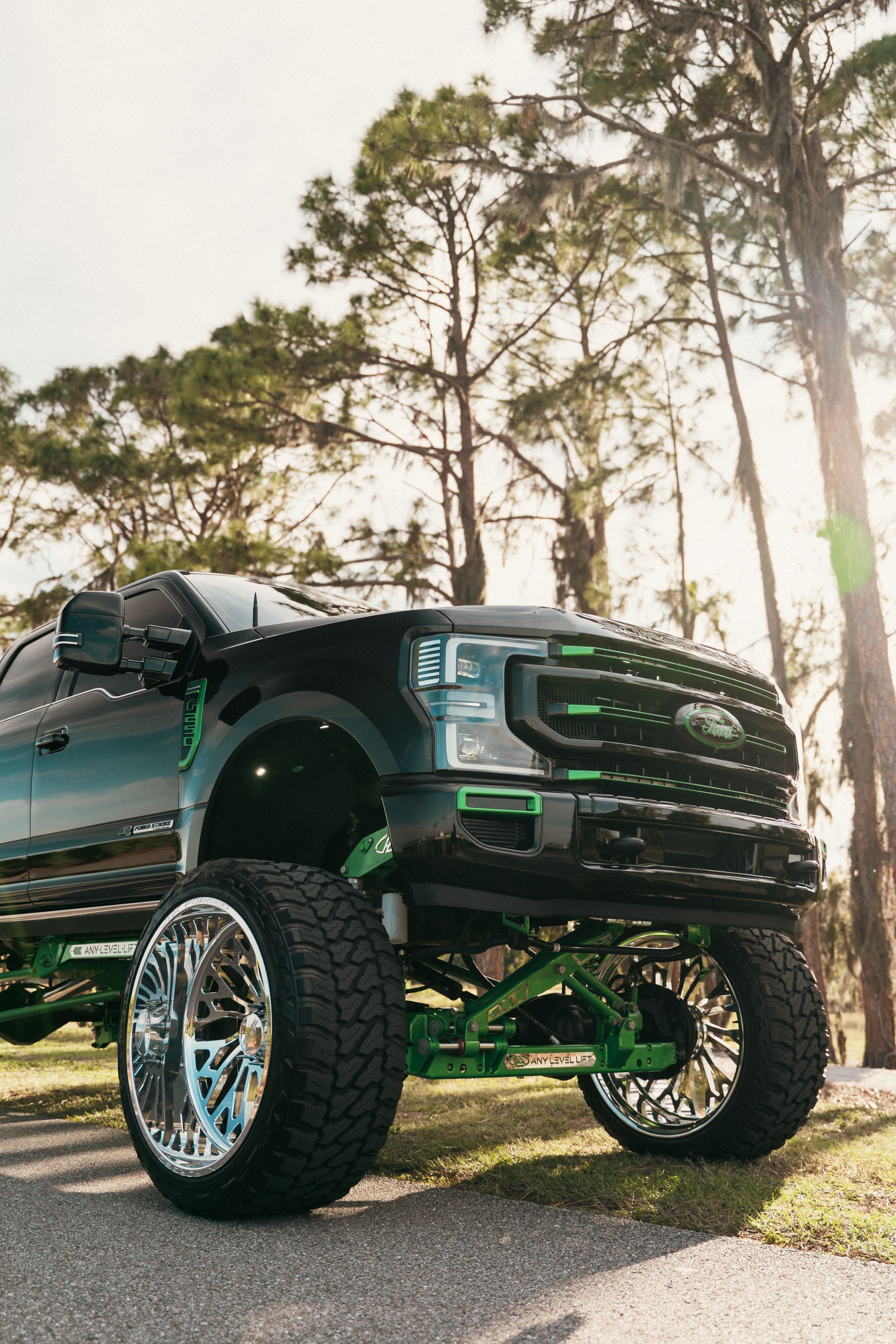 Black and green lifted Ford truck with large chrome wheels, parked outdoors.