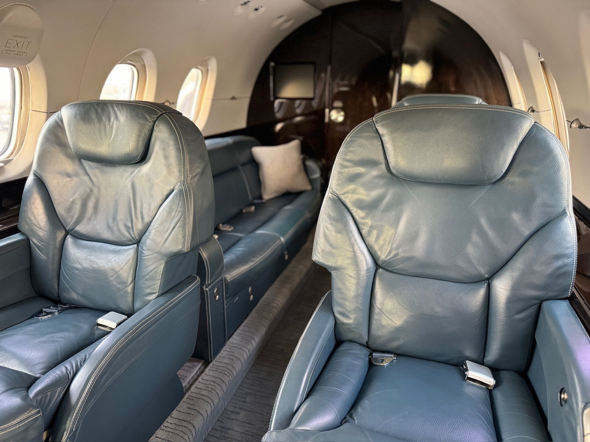 Interior of a private jet cabin with two blue leather seats and a bench seat; dark wood paneling.