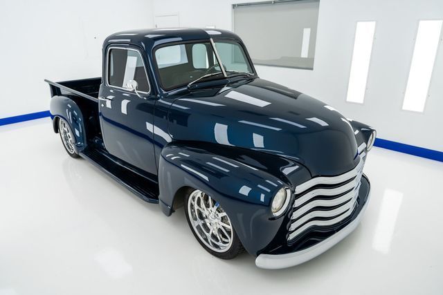 Dark blue classic pickup truck with chrome grill and wheels in a white studio.