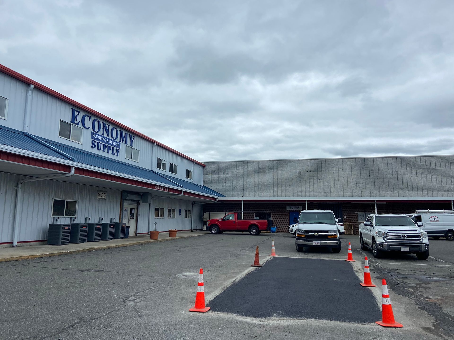Warehouse building with a parking lot featuring a freshly paved rectangular patch surrounded by orange cones.