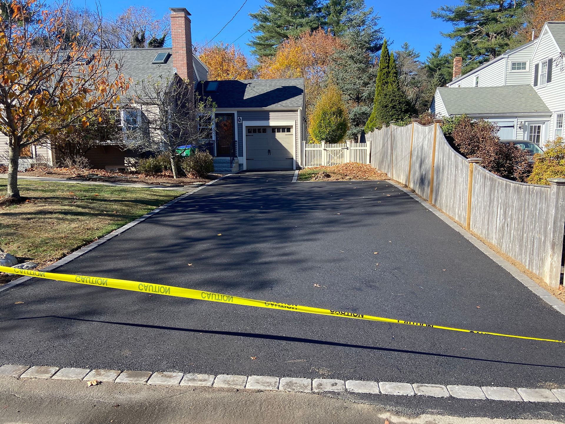 A newly paved asphalt driveway with a stone border in front of a house, marked off by yellow caution tape.
