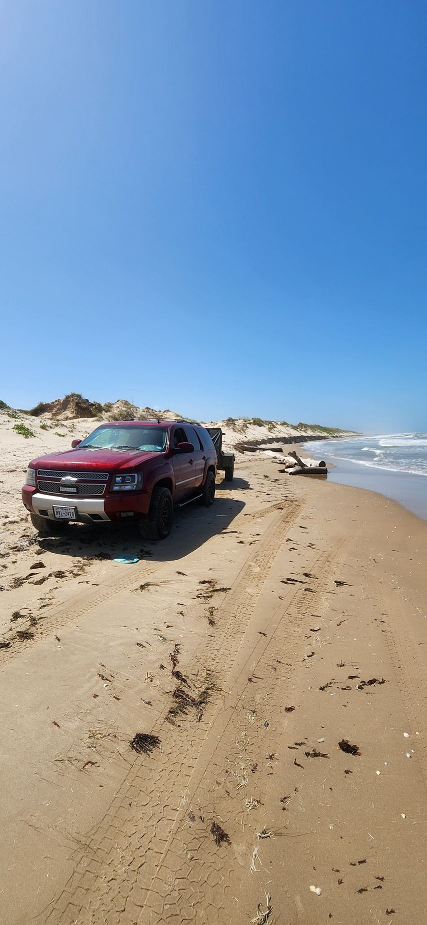 A red SUV parked on a sandy beach with the ocean in the background under a clear blue sky.