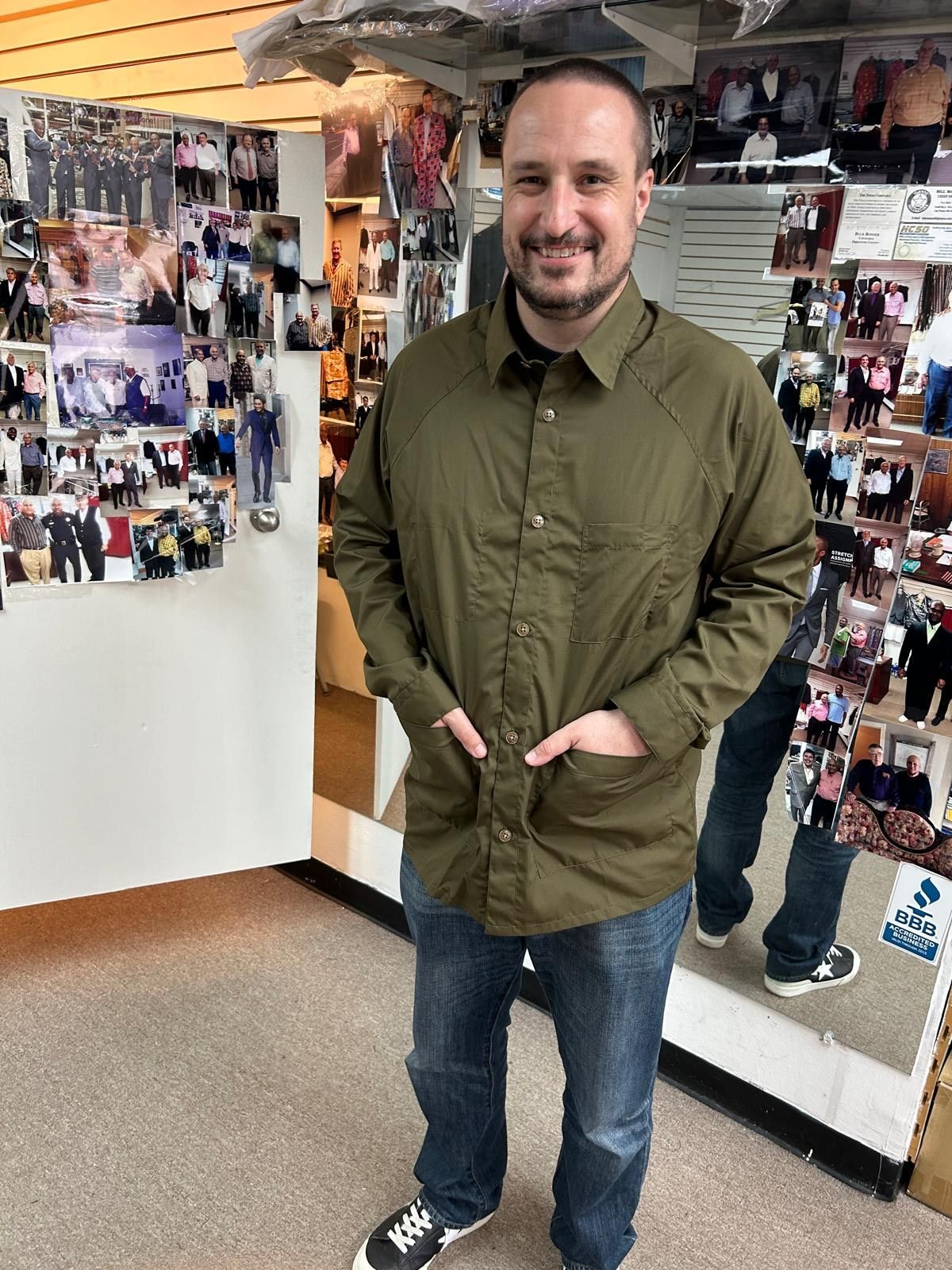 A man in a green shirt is standing in front of a wall of pictures.