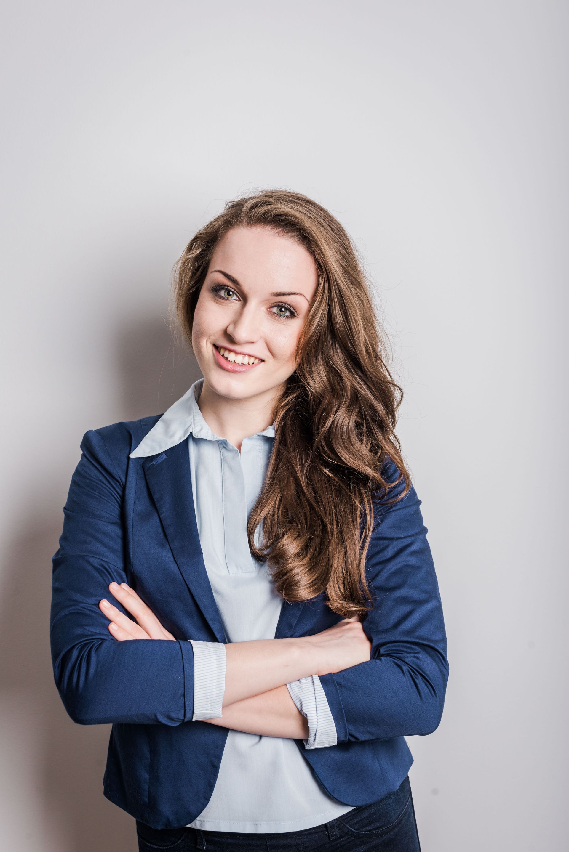 A woman in a blue jacket is standing with her arms crossed and smiling.