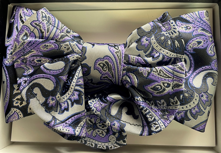 A purple and black paisley bow tie is in a box.