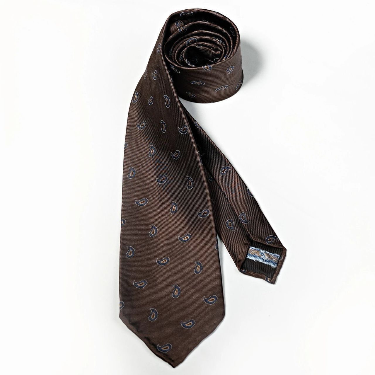 A brown tie is rolled up on a white surface