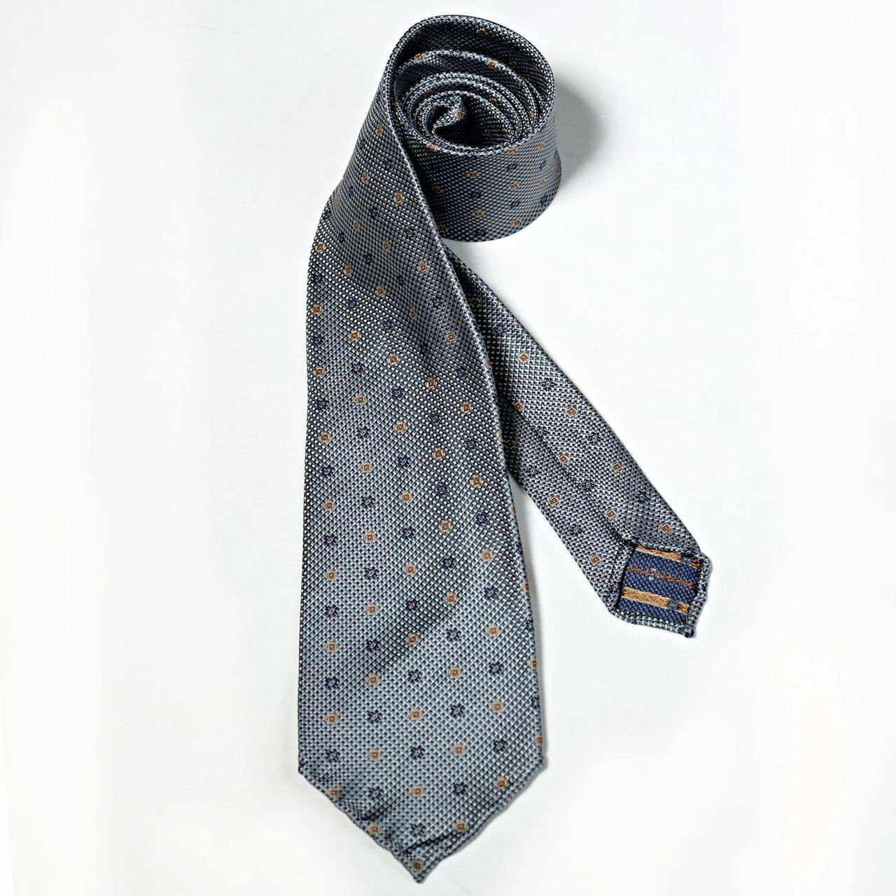 A blue tie with polka dots is rolled up on a white surface