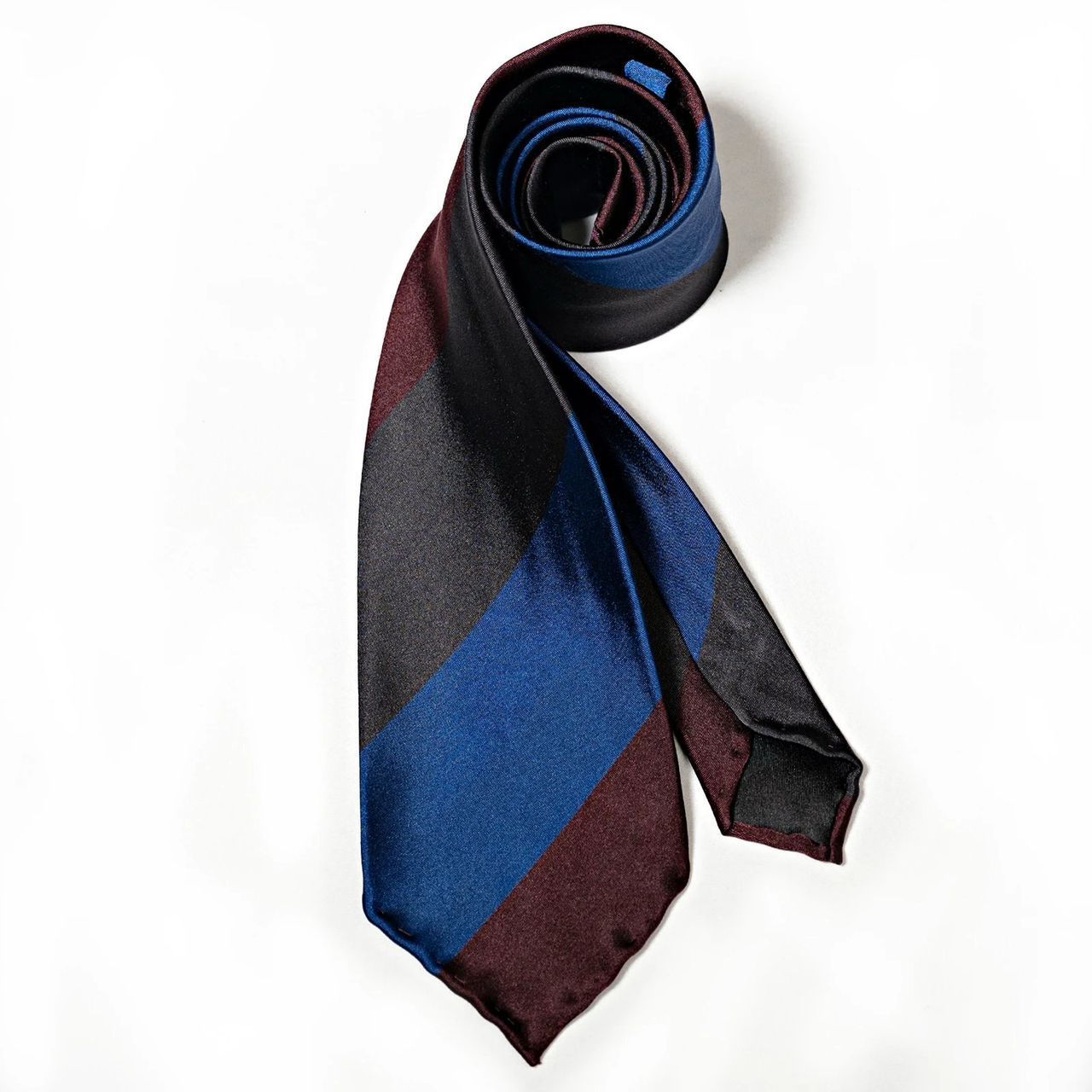 A blue and burgundy striped tie is rolled up on a white surface