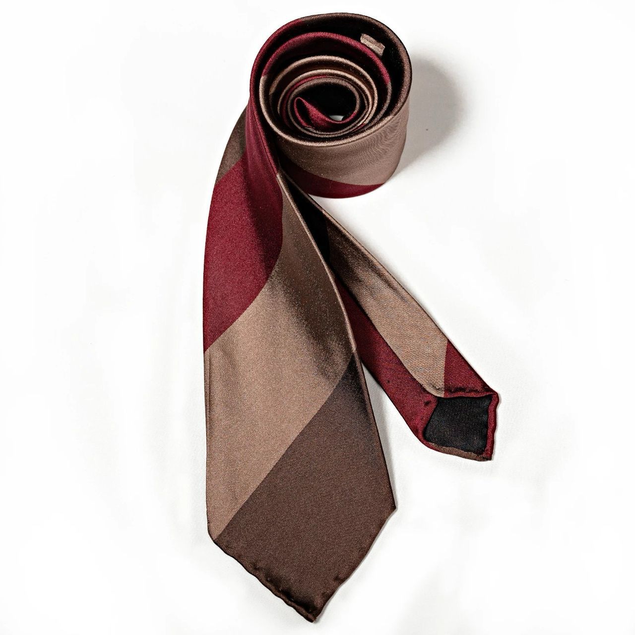 A brown and red tie is rolled up on a white surface