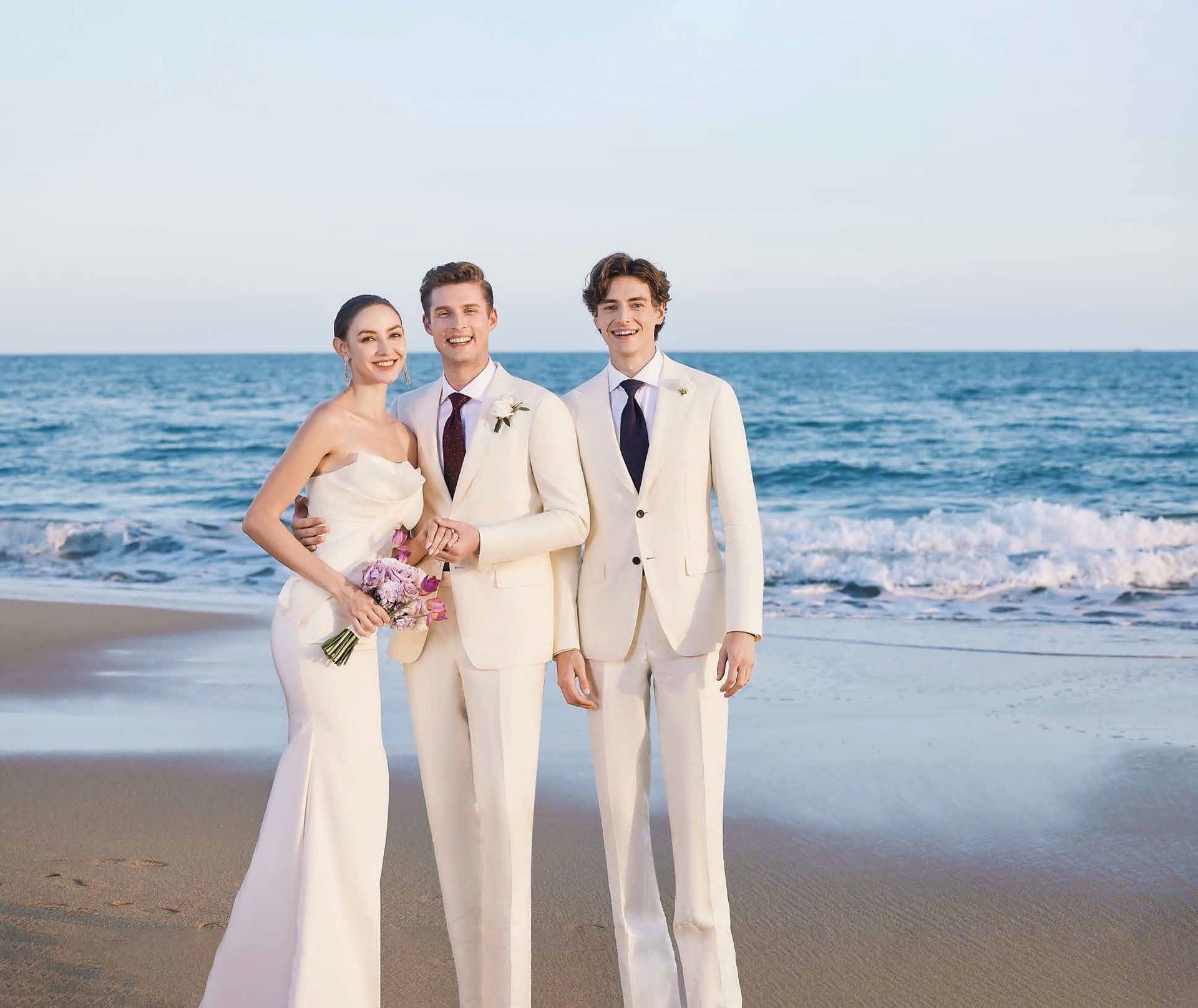 A bride and groom pose with their groomsmen on the beach