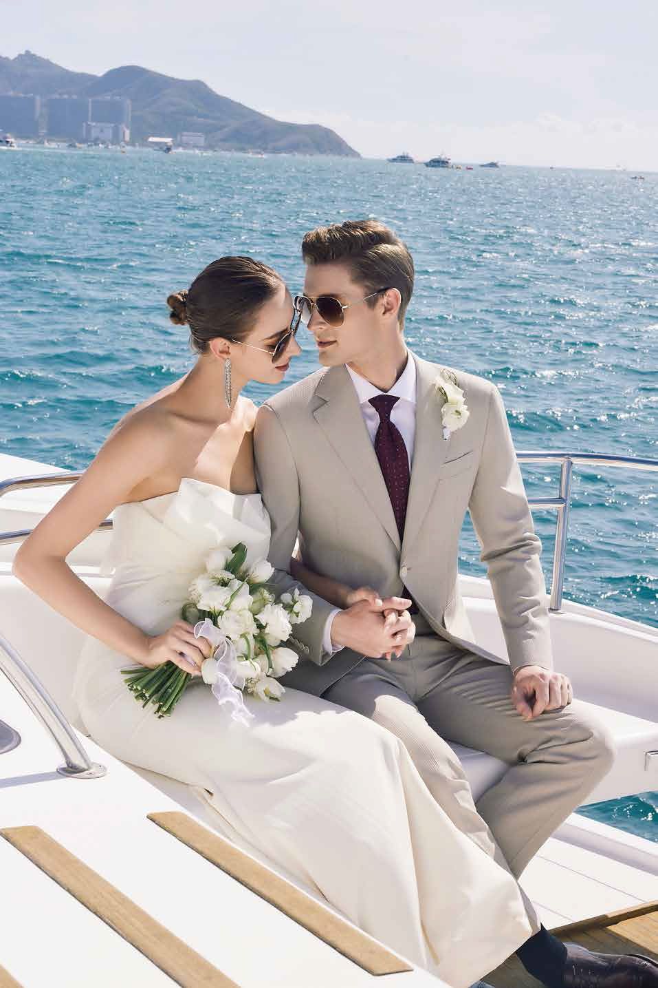 A bride and groom are sitting on a boat in the ocean holding hands.