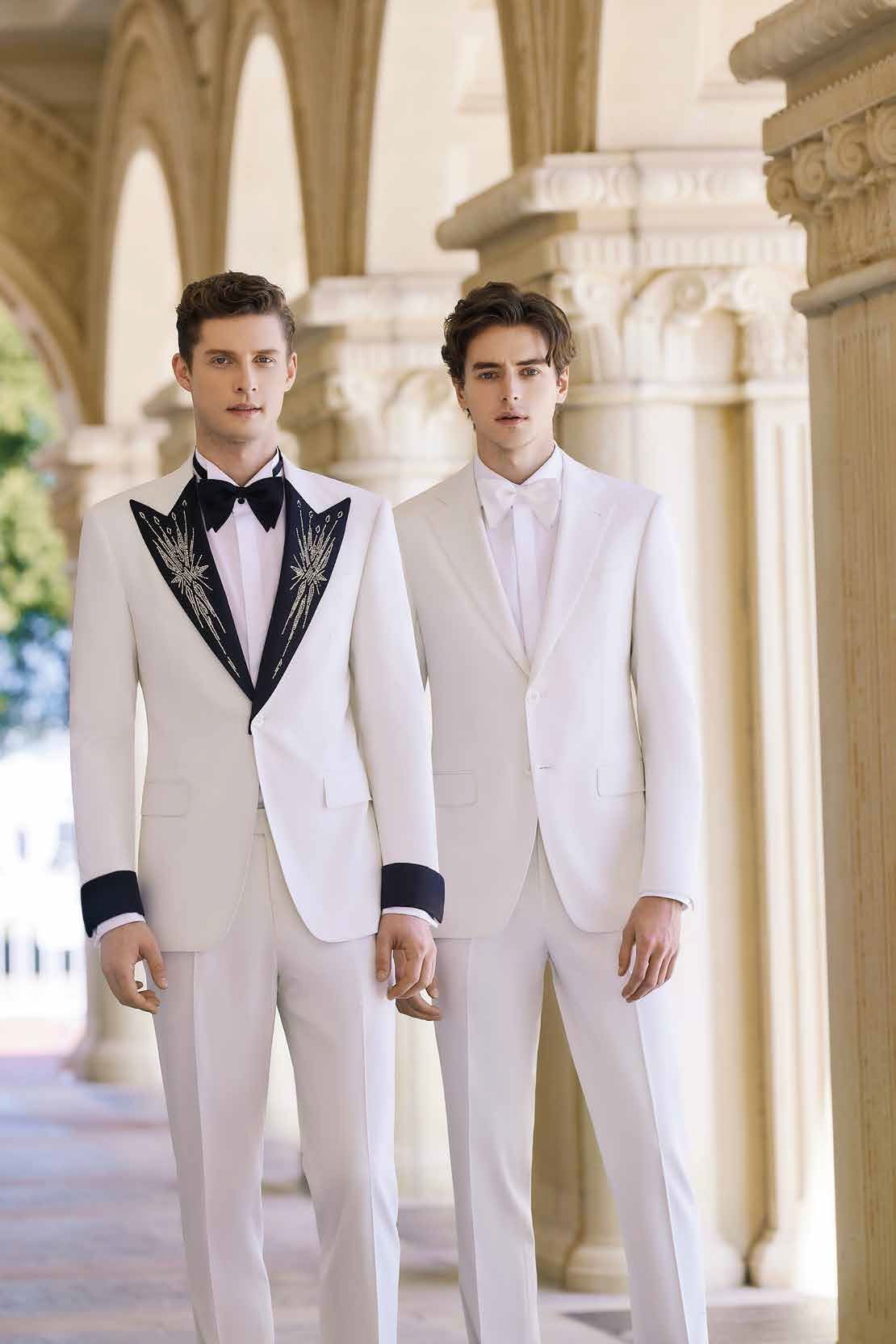 Two men in white suits are standing next to each other holding hands.