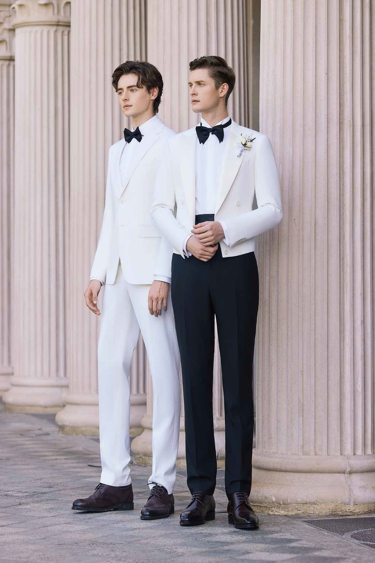 Two men in tuxedos are standing next to each other in front of a building.