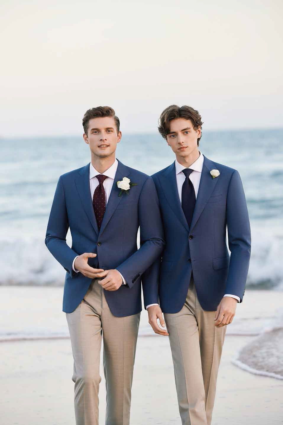 Two men in suits and ties are standing next to each other on the beach.