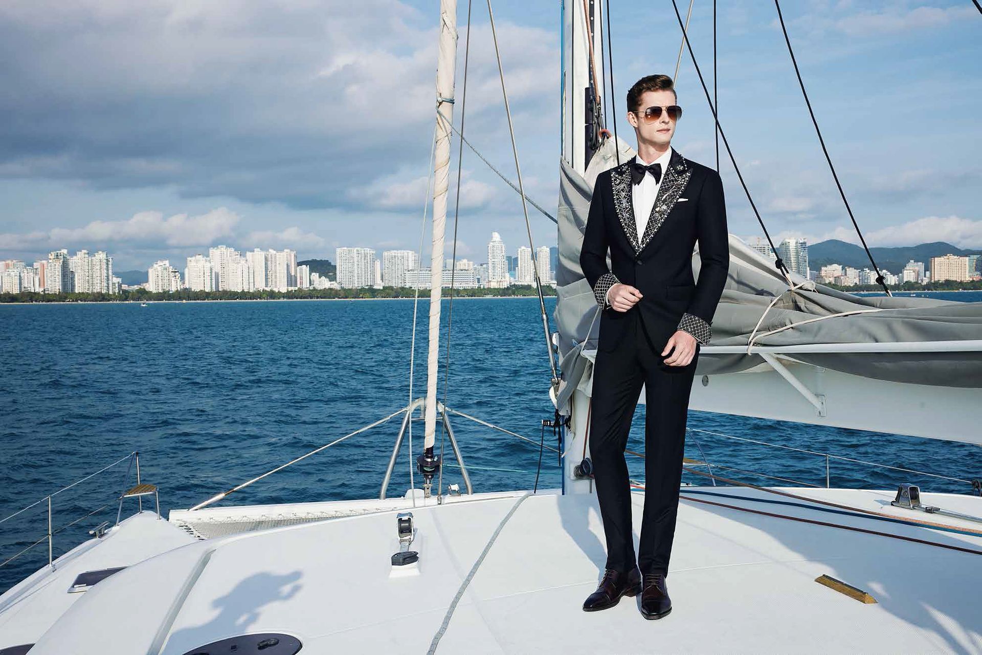 A man in a suit is standing on the deck of a sailboat in the ocean.