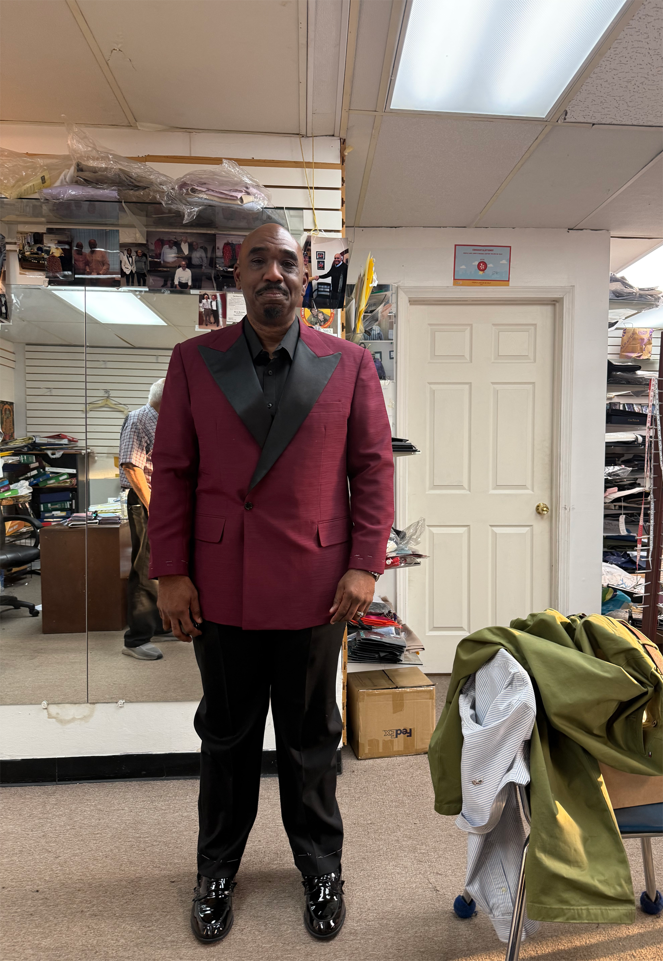 Man in a maroon blazer, black shirt, and pants stands in a shop with mirrors and clothing racks.