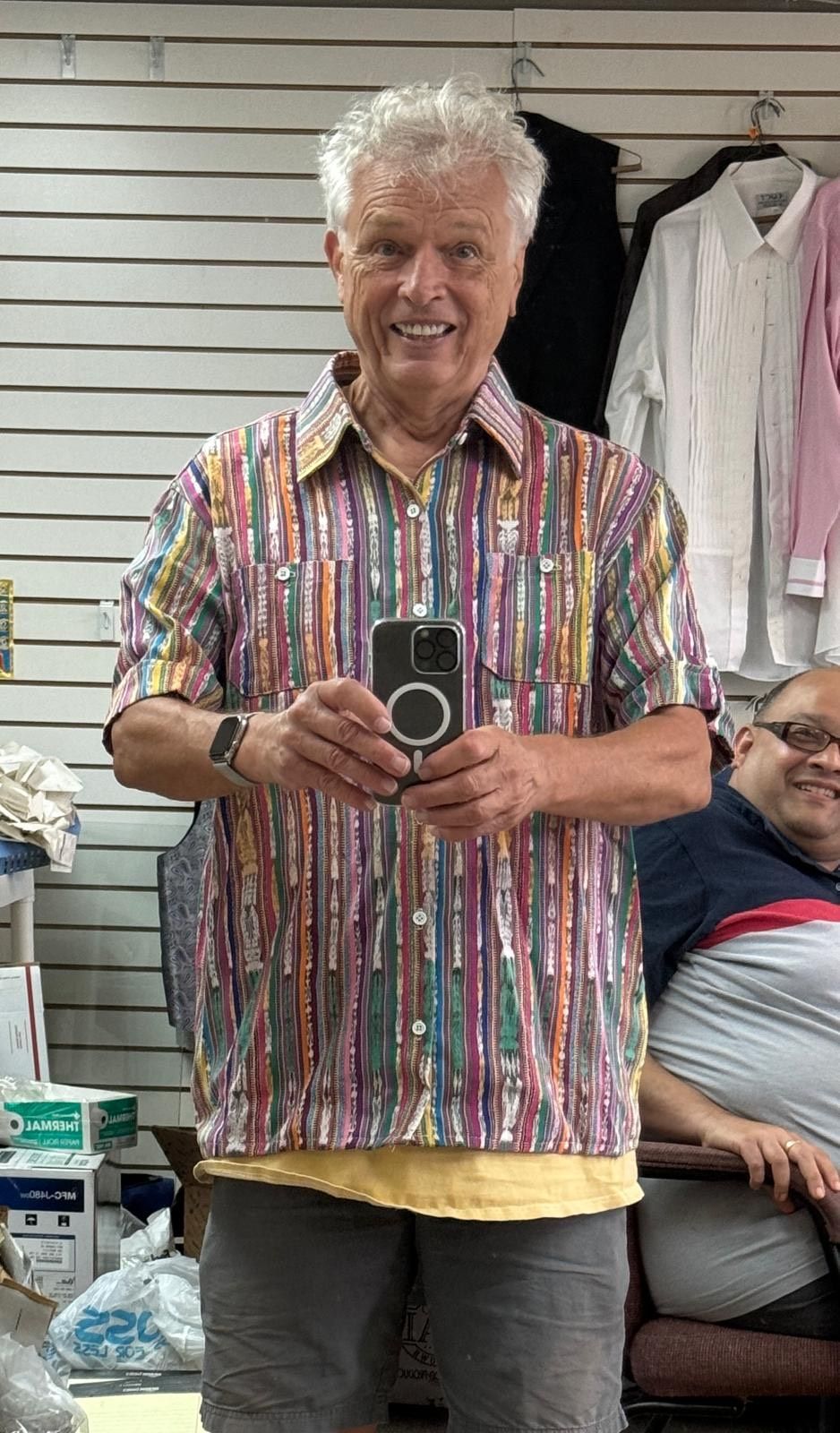 A man in a colorful shirt is taking a picture of himself in a mirror.
