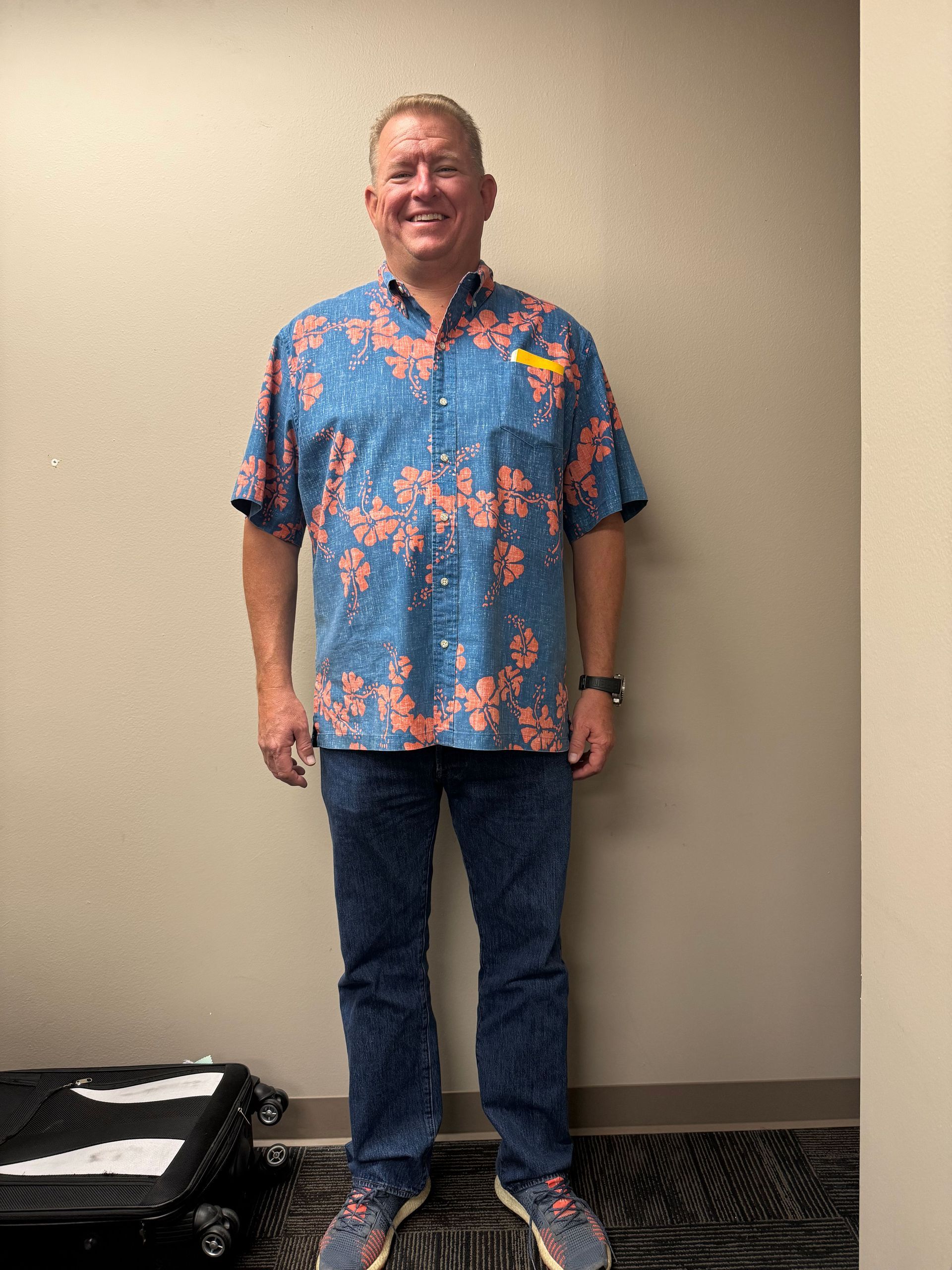 A man wearing a blue hawaiian shirt and jeans is standing in a room.
