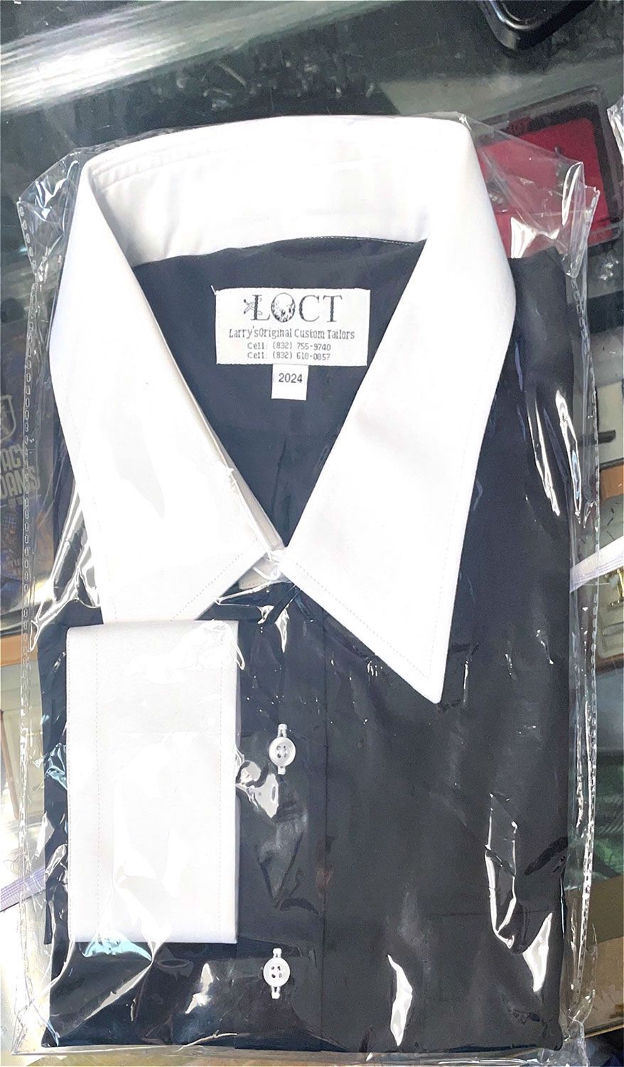 A black shirt with a white collar is in a plastic bag