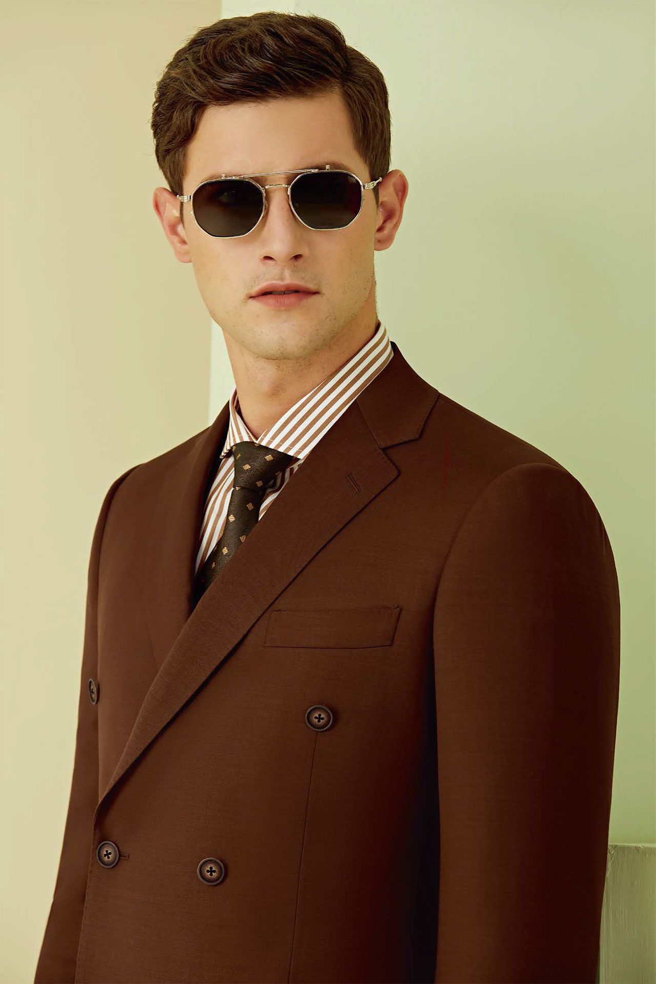 A man in a brown suit and tie is wearing sunglasses