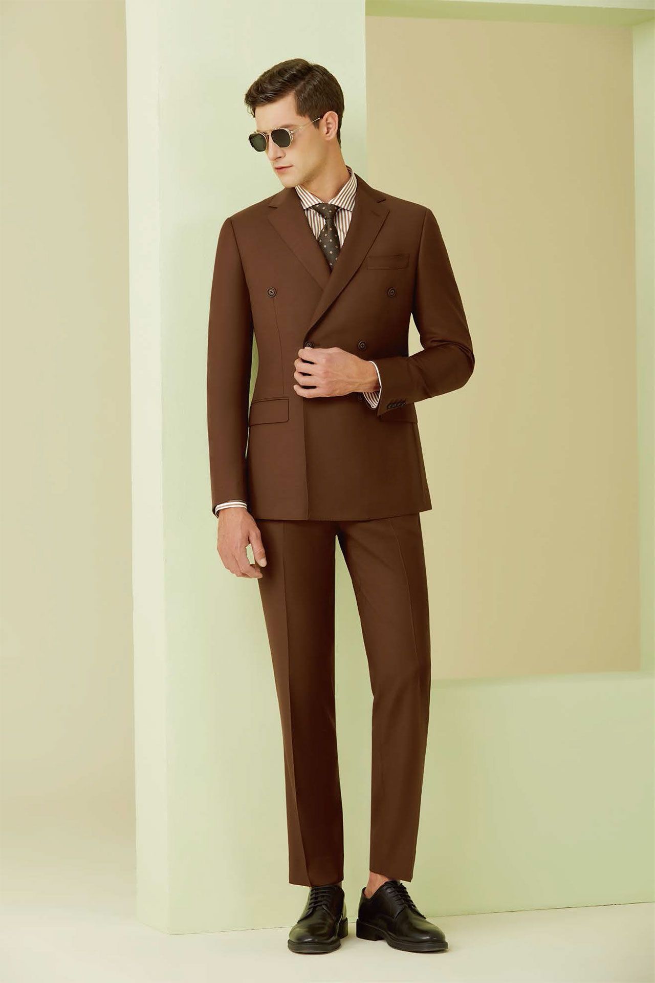 A man in a brown suit and tie is standing next to a wall