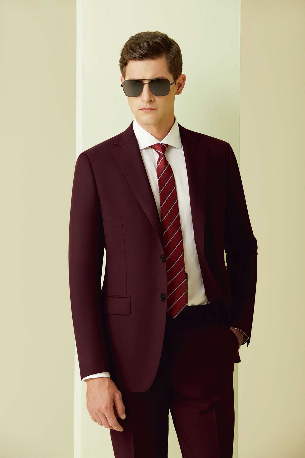 A man in a maroon suit and tie is wearing sunglasses