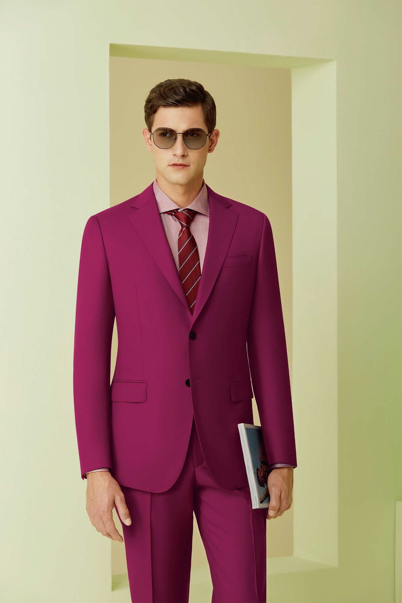 A man in a dark pink suit and tie is holding a book