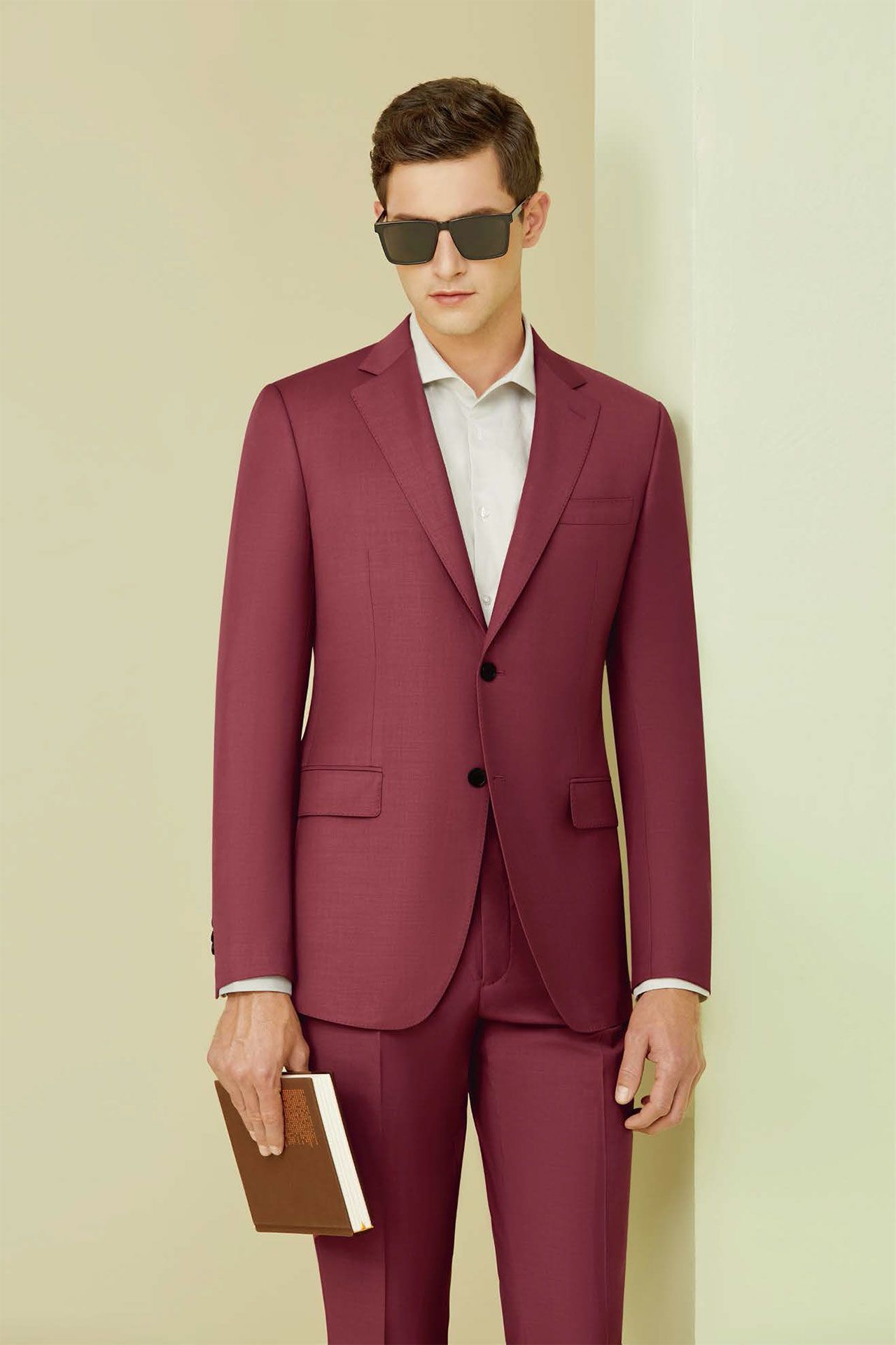 A man in a maroon suit and sunglasses is holding a book