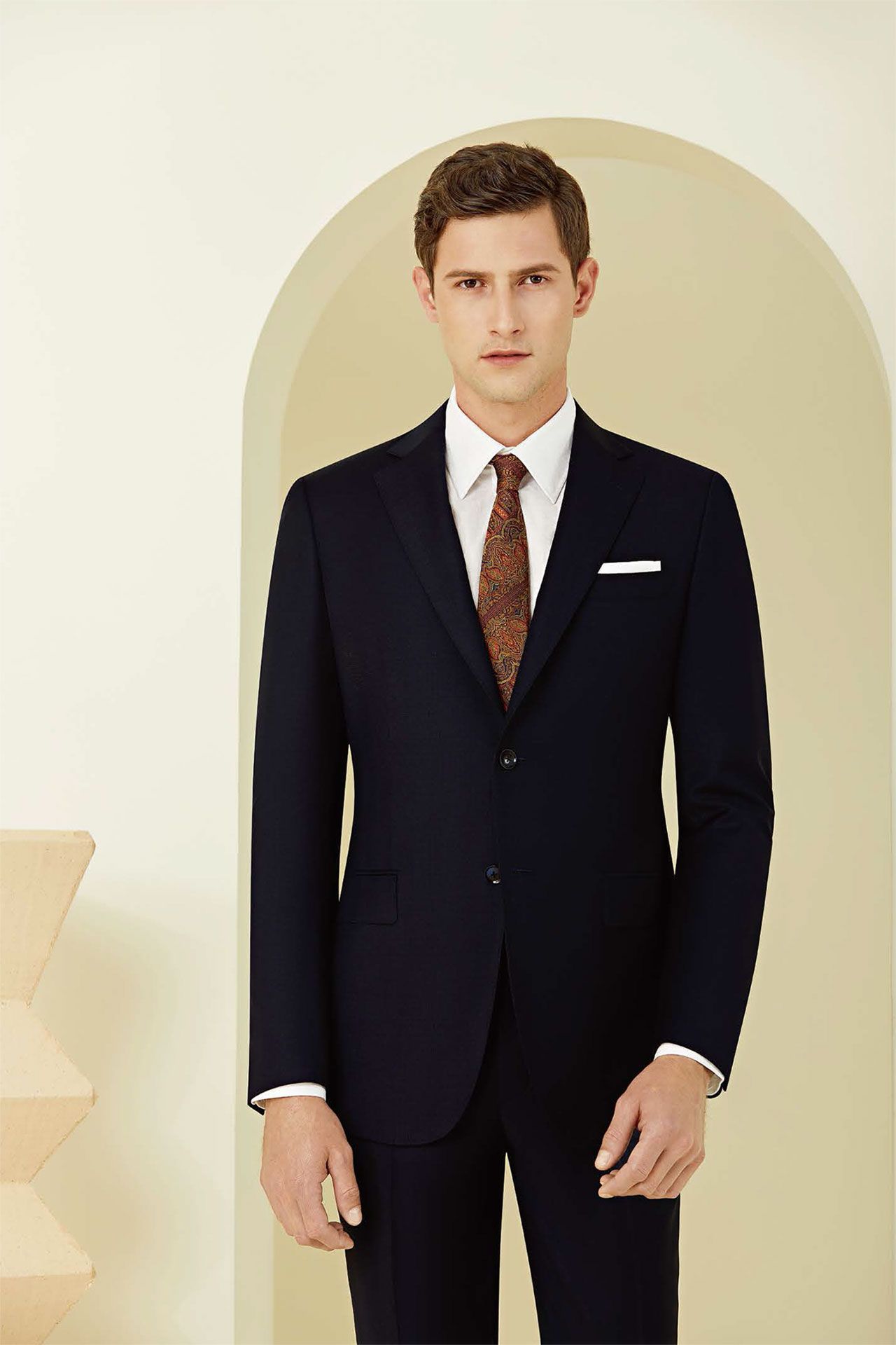 A man in a suit and tie is standing in front of a wall