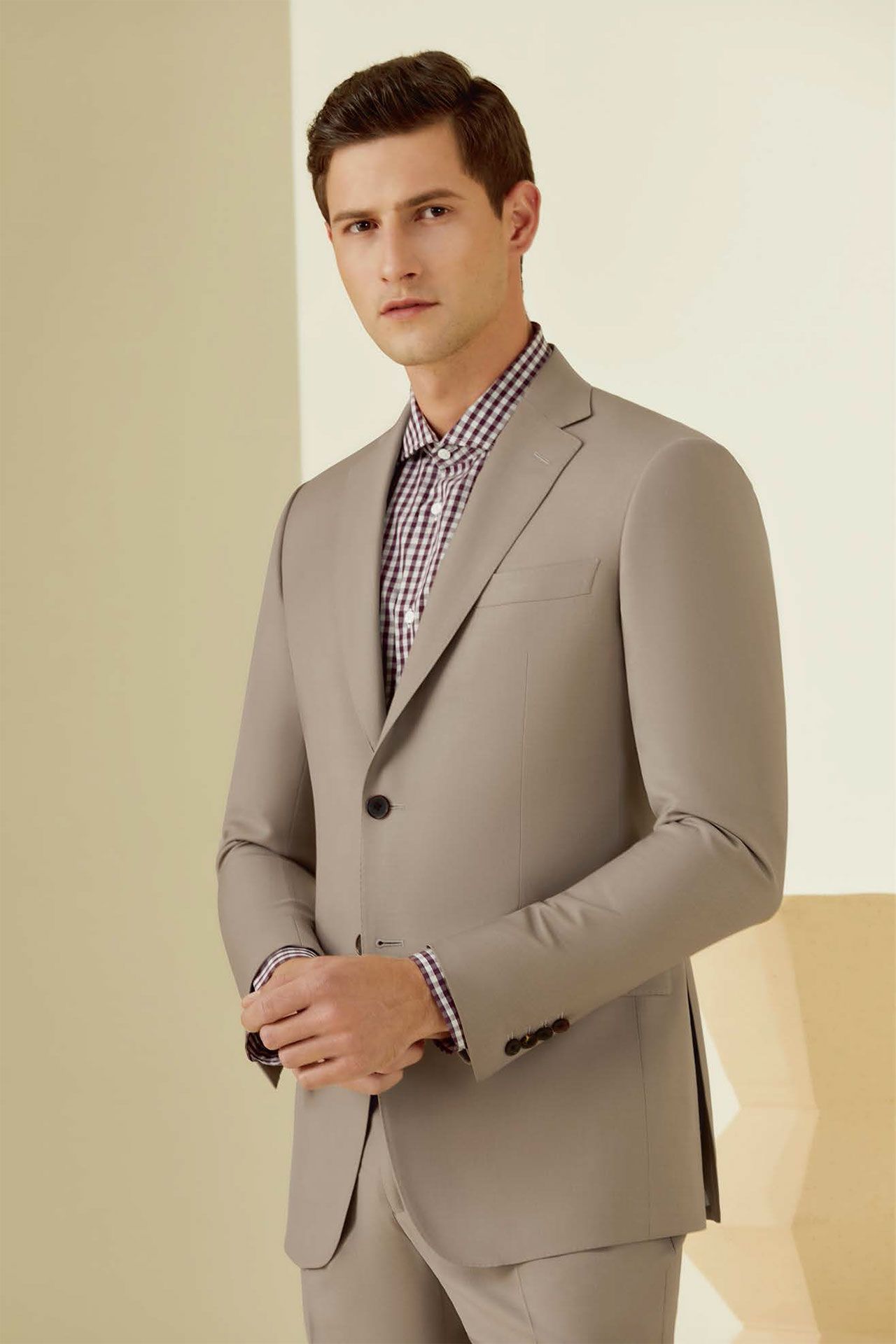 A man is wearing a tan suit and a plaid shirt