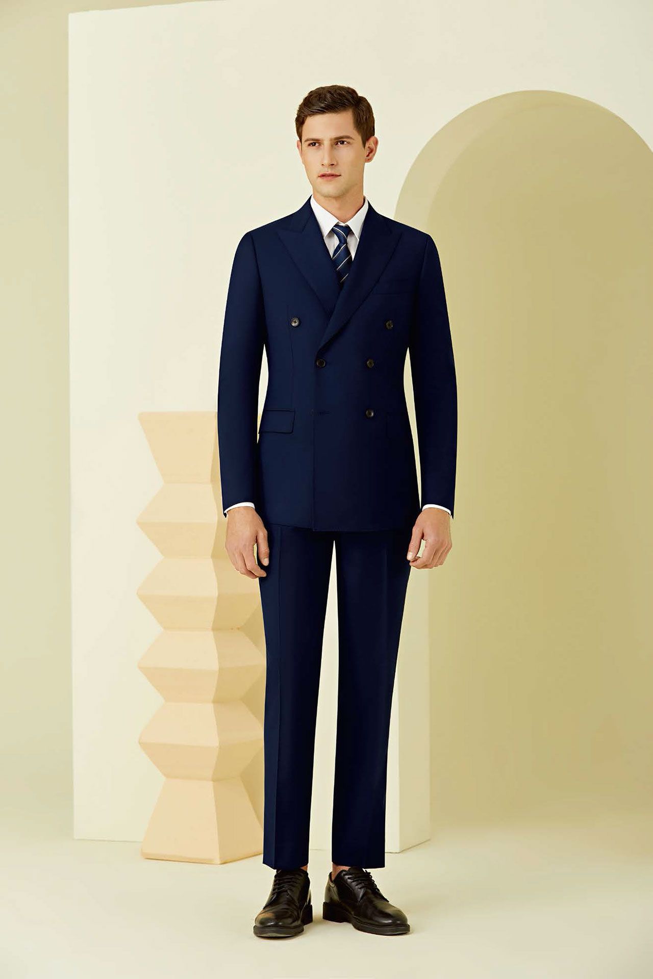 A man in a blue suit and tie is standing in front of a wall