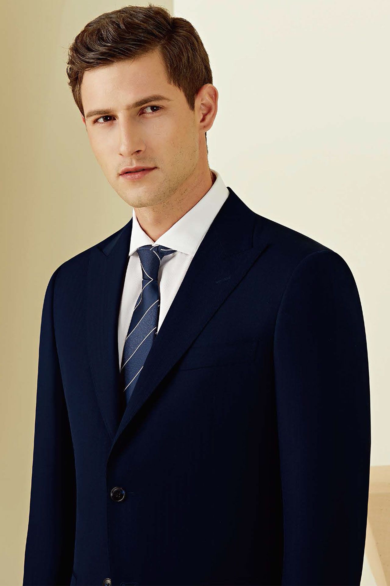 A man in a suit and tie is standing in front of a wall